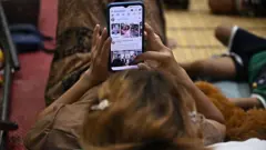 Женщина смотрит на экран телефона, фото сделано со спины и ее лица не видно