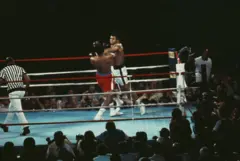O campeão dos pesos pesados, George Foreman (de sunga vermelha), e o desafiante Muhammad Ali competem na luta pelo título mundial de pesos pesados, conhecida como 'Rumble in the Jungle'