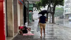 Uma mulher se abriga sob um guarda-chuva enquanto passa por moradores de rua durante um dia chuvoso no Rio de Janeiro, em 22 de março de 2024.