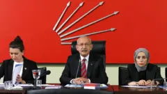 Kemal Kılıçdaroğlu ortada duruyor. Sol yanında başörtülü bir üye var, diğer tarafında ise başı açık bir kadın elindeki dosyaya baklıyor.