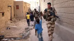 Soldats français salués par des enfants dans une rue au Mali.