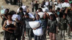 فلسطينيون يحملون مساعدات، في بيت لاهيا، شمال قطاع غزة، 2 أغسطس/آب 2025.
