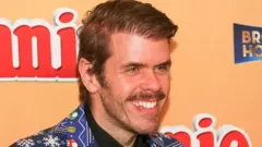 Perez Hilton sonríe mientras asiste a un evento en Hollywood en noviembre de 2022. Lleva un traje azul vibrante con un patrón llamativo que incluye copos de nieve y personajes de Super Mario