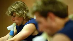 Dois atletas sentados sopram em tubos para avaliar sua capacidade pulmonar