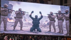 Иранцы с флагами своей страны смотрят на огромный экран, на котором изображено задержание боевика ИГ иранскими военными КСИР, фото сделано в ноябре 2025 г.