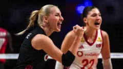 Gizem Orge siyah formasıyla sağ kolunu katlayarak güç işareti yapıyor, sevinçe haykırırken görünüyor, geride beyazlı takım arkadaşı flu. 
