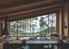 Sala de estar con estructura de madera, chimenea suspendida y ventanales panorámicos con vista a un lago entre pinos.