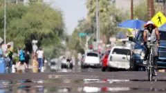Uma pessoa pedala enquanto ondas de calor provocam distorções na imagem. Ao fundo, outras pessoas caminham pela rua