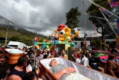 Personas llevan a hombros un féretro que pasa por delante de una atracción de feria de Bob Esponja.