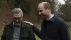 Eugene Levy, Prince William and walking in the park. William is laughing and has his hand on Eugene's shoulder
