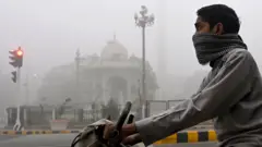 covek na motoru sa maramom preko lica se stiti od otrovnog smoga u pakistanu