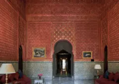 Fotografía interior de un palacio con paredes rojas elaboradamente talladas, detalles de azulejos y muebles rojos.