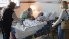 A woman in a hospital bed surrounded by two other women and a man