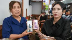 Duas mulheres, uma mais velha e outra mais jovem, estão sentadas em um café segurando celulares com imagens de um homem mais velho.