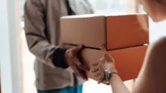A man passes two brown boxes to a woman.
