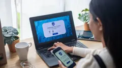 Mulher jovem de costas digitando uma senha no laptop