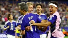 青色ユニホームの前田がチームメートと抱き合って笑顔を見せている。他の日本選手らも近くで笑顔を見せている