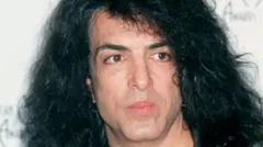 Paul Stanley posando para foto em evento, na frente de painel