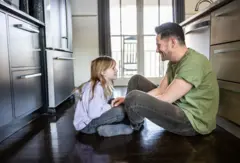 Uma menina e um homem sentados no chão, olhando um para o outro e rindo