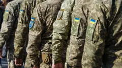 Група військовослужбовців у піксельному камуфляжі, які стоять у строю. На рукавах форменого одягу видно нашивки з прапором України та тризубом.