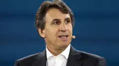 O empresário Marc Rowan olhando para a direita com um microfone preso ao rosto, vestido com um terno preto e sentado em frente a um fundo azul.