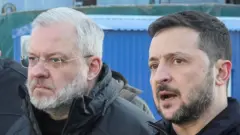 黒っぽい上着姿の男性二人が屋外で、横並びで斜め前方を見ている。ゼレンスキー氏は話している様子で口を開いている