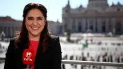 Alvarado sosteniendo un micrófono de EWTN y de fondo la plaza y la Basílica de San Pedro.