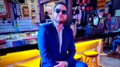 Paul Flores sentado em um bar de óculos escuros