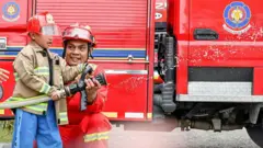 Foto ilustrasi. Seorang petugas pemadam kebakaran memberi contoh cara menyemprotkan air kepada seorang siswa sekolah.