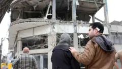 Moradores reagem à sua residência danificada ao lado de um prédio comercial que inclui escritórios da emissora qatari Al Araby TV, após um ataque aéreo no norte de Teerã