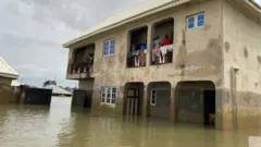 Mutane tsaye a hawa na sama na gidan  Mohammed Sani Gambo