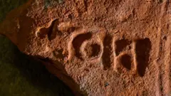 Uma telha vermelha com um 'carimbo' composto por três letras em sua superfície mostrando que era um prédio público e pertencia ao procurador de Londres. Também tem uma série de ranhuras curvas feitas pelo fabricante da telha, arrastando seus dedos sobre ela quando estava sendo produzida