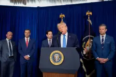 الرئيس الأمريكي، دونالد ترامب، في مؤتمر صحفي يرتدي بذلة زرقاء ورابطة عنق وخلفه عدد من المسؤولين الأمريكيين، من بينهم وزير الدفاع الحرب الأمريكي، بيت هيغسيث، ووزير الخارجية، ماركو روبيو.