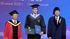 Николай Лукашенко в шапочке и мантии выпускника, с дипломом на сцене между двумя мужчинами