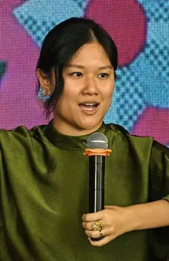 Karen Hao usando um vestido verde e segurando um microfone