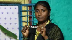 Ankita, uma jovem devadasi, exibe seu colar de pérolas. Ela veste um vestido amarelo estampado e um xale preto.