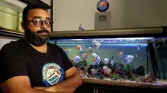 Aquarista Antonio Candido com um aquário atrás e peixes coloridos