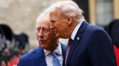 Kral 3. Charles ve Trump karenin solunda bir yere dikkatlice bakıp bir şeyler konuşuyorlar. 