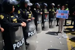 Una manifestante sostiene un cartel en el que dice "Vizcarra no está solo" frente a una línea de policías antimotines, quienes sostienen escudos plásticos.