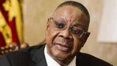 A close-up shot of Peter Mutharika wearing silver-rimmed glasses and a suit