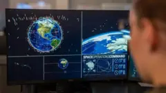 Soldado olha para tela de computador mostrando o planeta Terra e objetos em sua órbita.