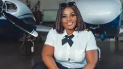 Tracy Olushola Atobatele knees before two aircrafts