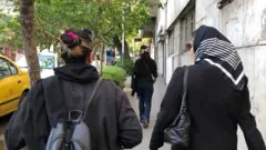 Deux femmes marchant dans une rue, l'une porte un foulard, l'autre non.
