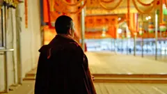 Um monge tibetano de costas durante as orações matinais no mosteiro de Kirti