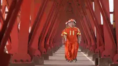 Vários trabalhadores vestidos de laranja em uma fábrica de petróleo na China.