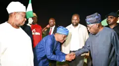 FCT Minister Nyesom Wike wear navy blue cloth and cap dey bow as e dey shake President Bola Tinubu hand as e land for abuja airport while oda goment officials dey look