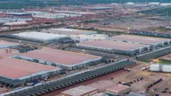 Prédios imensos estão em construção, com guindastes e andaimes visíveis ao longo da paisagem.