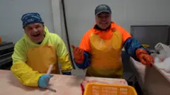 O mexicano Edgar Vega e uma colegasite de bolao loteriatrabalho aparecem na fotosite de bolao loteriauma peixaria, ambos rindo, usando boné e bandana, luvassite de bolao loteriaborracha e casaco. 