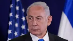 Benjamin Netanyahu com olhar sério, em frente a bandeiras