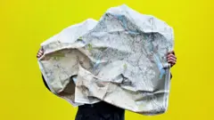 Зображення людини, схованої за великою мапою, яку вона тримає в руках, на жовтому тлі